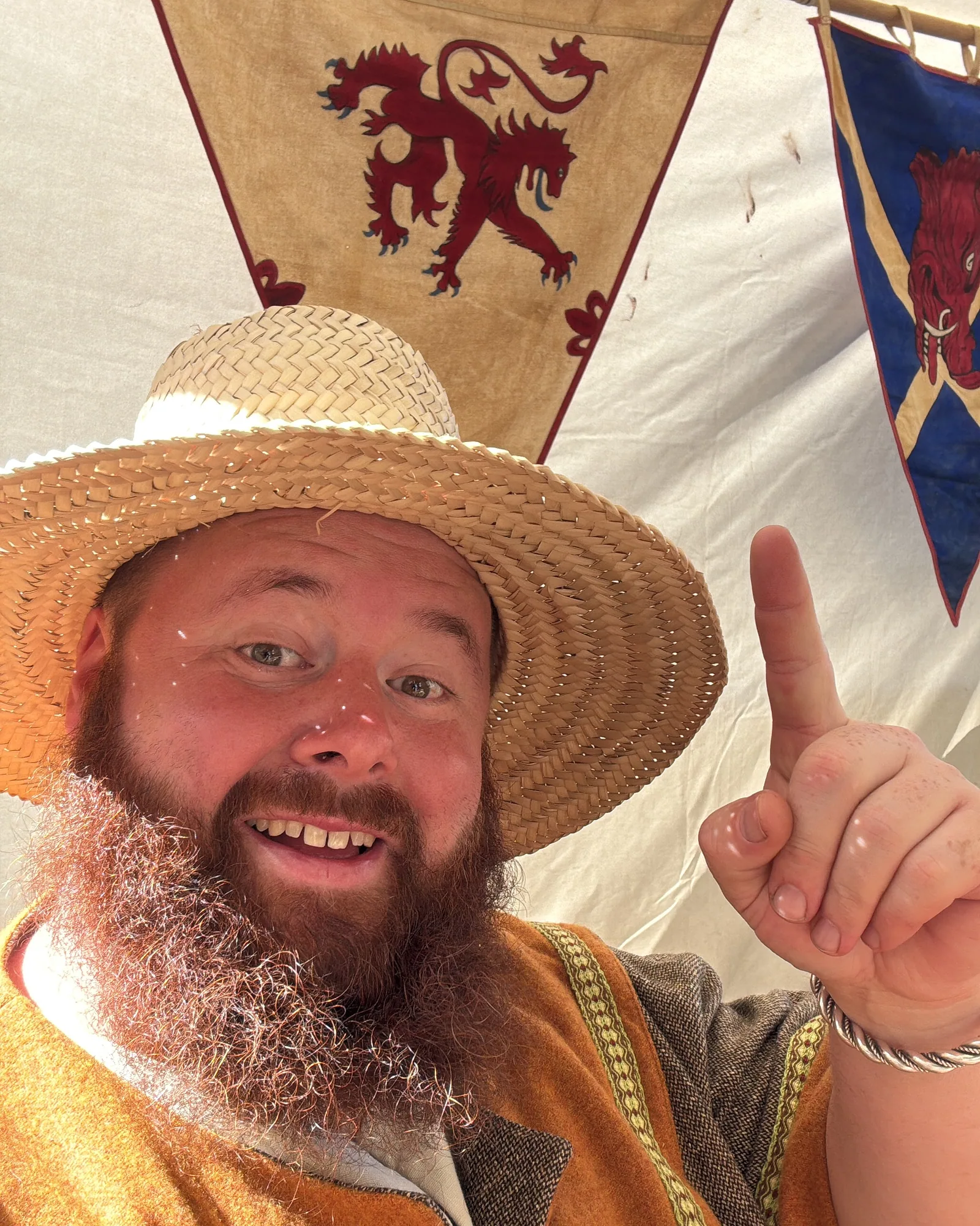 Robin mit Strohhut und Wollgewand lachend vor den Wappenbannern im Lagerzelt